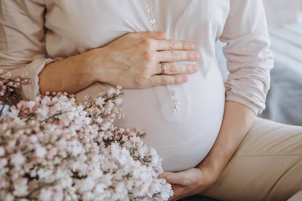妊娠中の女性は 新鮮な花の背景に手で彼女の腹を保持しています — ストック写真