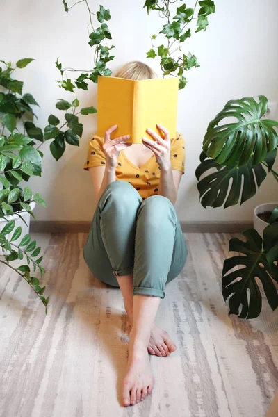 woman reading book yellow lining room flowers