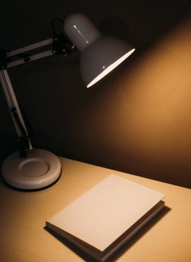 Masanın altındaki karanlık bir ofisteki bir masada kitap. Sarı ışık ve gölge.