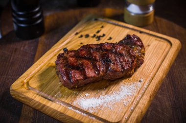 Izgara domuz kaburga pirzola biftek bir kil plaka yağ, hardal, tuz ve biberiye ile eski bir ahşap tablodur.