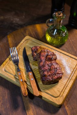 Çatal ve bıçak otlar baharatlar ve tuz ahşap tahta üzerinde sulu orta dana kaburga eti.