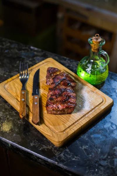 Šťavnaté střední hovězí Rib Eye steak na dřevěné desce s vidličkou a nožem bylinky koření a sůl. — Stock fotografie