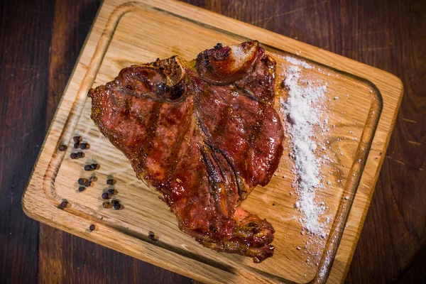 Chuleta de chuleta de cerdo a la parrilla en un plato de barro con aceite, mostaza, sal y romero es una mesa de madera vieja . — Foto de Stock