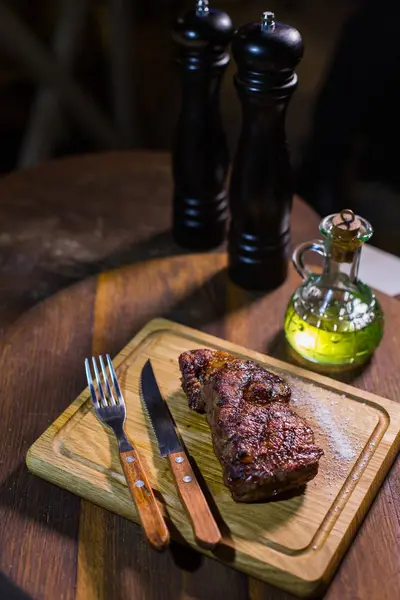 Šťavnaté střední hovězí Rib Eye steak na dřevěné desce s vidličkou a nožem bylinky koření a sůl. — Stock fotografie