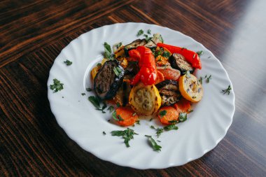 ahşap bir masa üzerinde beyaz bir tabak üzerinde ızgara sebze