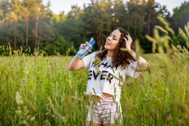 Kıvırcık saçlı kız sıcak bir günde tarlada su içer..