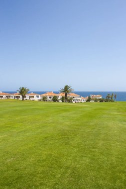 Atlantik Okyanusu yakınlarındaki lüks sahil otel tatil Golf Sahası. Yeşil çim sahası, palmiye ağaçları, ev, mavi gökyüzü ve okyanus