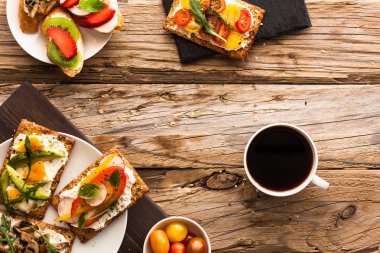 Kahvaltı Masası lezzetli bruschetta crostini tost, krem peynir, taze sebze ve meyve ve bir fincan sade kahve. Sabah heathy dengeli beslenme. Rustik ahşap arka plan üzerinde renkli maddeler