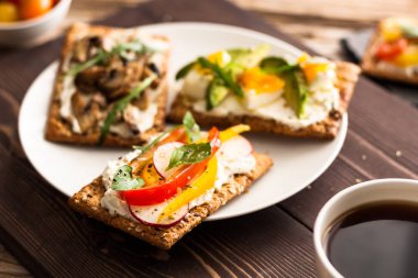 Kahvaltı Masası lezzetli bruschetta crostini tost, krem peynir, taze sebze ve meyve ve bir fincan sade kahve. Sabah heathy dengeli beslenme. Rustik ahşap arka plan üzerinde renkli maddeler