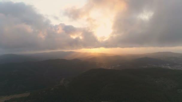 密な暗い山林にゆっくりと下って飛んでいく 雲の美しい景色と太陽の光のビームと素晴らしいゴールデンアワーの夕日 空中映画4Kドローン映像 — ストック動画