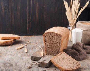 Kepekli ekmek. Mayasız kepekli ekmek unu, buğday taneleri, spikelets ahşap bir kahverengi masa üzerinde bir kesme tahtası üzerinde. Bir somun ekmek parçalar halinde kesilerek. Uzay kopyalayın. Koyu arka plan. Ev yapımı. 
