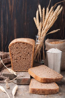 Kepekli ekmek. Mayasız kepekli ekmek unu, buğday taneleri, spikelets ahşap bir kahverengi masa üzerinde bir kesme tahtası üzerinde. Bir somun ekmek parçalar halinde kesilerek. Uzay kopyalayın. Koyu arka plan. Ev yapımı. 