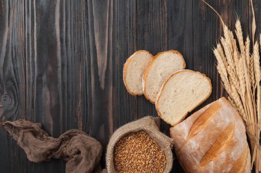 Ekmek. Buğday taneleri ve buğday spikelets bir çanta ile kahverengi ahşap bir masa üzerine dilimlenmiş beyaz buğday ekmeği loafs. Üstten görünüm. Uzay kopyalayın. Rustik.