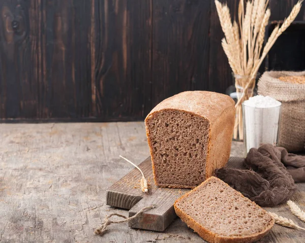 Kepekli ekmek. Mayasız kepekli ekmek unu, buğday taneleri, spikelets ahşap bir kahverengi masa üzerinde bir kesme tahtası üzerinde. Bir somun ekmek parçalar halinde kesilerek. Uzay kopyalayın. Koyu arka plan. Ev yapımı. 