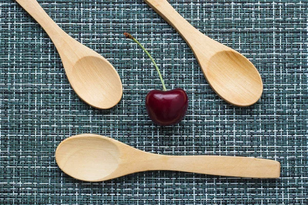 Ripe cherry on a wicker background and three wooden spoons, close-up