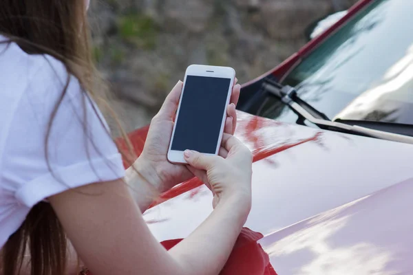 Bir smartphone bir araba kaputun üstünde tutan bir kız Close-up