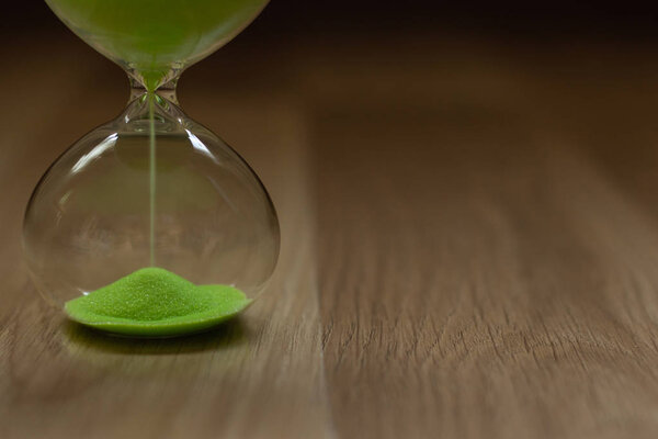 close-up, hourglass with green sand on a wooden background