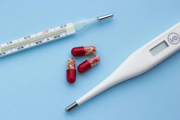 Electronic and mercury thermometer with red-yellow pills on a blue background