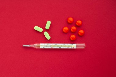 Mercury termometre ile kırmızı bir arka plan, sağlık kavramını turuncu ve yeşil tablet