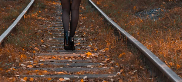 Beautiful female feet on the railway tracks, near the fallen leaves