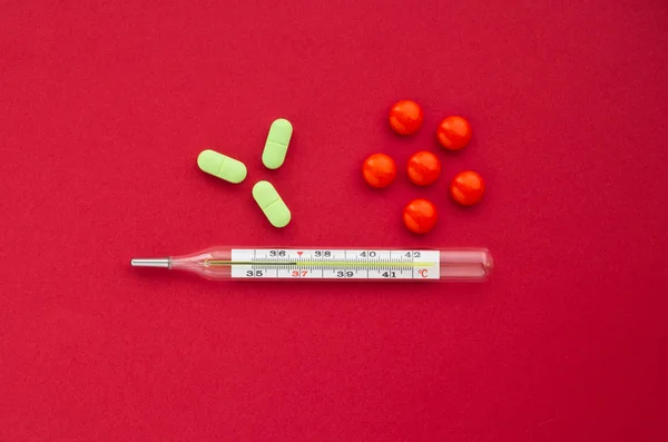 健康の概念 赤の背景にオレンジ色と緑色の錠剤で水銀温度計 — ストック写真
