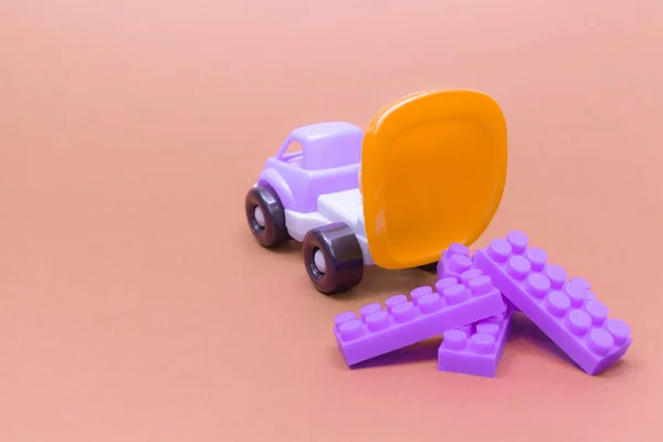 Caminhão de brinquedo descarrega os detalhes dos blocos em um fundo rosa — Fotografia de Stock