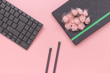 Üst görünüm, pembe arka planda klavye ile çiçek ve kalem ile defter. Düz yatlı stil