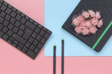 Üst görünüm, pembe ve mavi arka planda klavye ile çiçek ve kalem ile defter. Düz yatlı stil