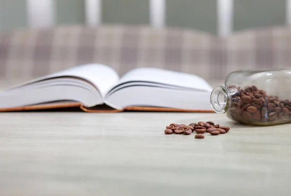 Un libro abierto sobre una mesa blanca y una botella de granos de café, el — Foto de Stock