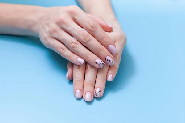 Belas mãos femininas e uma manicura na moda em um fundo azul — Fotografia de Stock