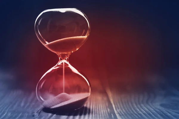 Modern Hourglass with dark background, sand trickling through the bulbs of a crystal sand glass, with red light in the center. Lost time concept — Stock Photo, Image