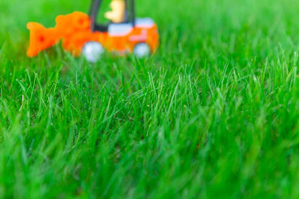 Blurred toy loader, truck on fresh green grass, toy for children. — Stock Photo, Image