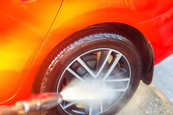 Lavando el coche y las ruedas con agua de alta presión, teñida con luz — Foto de Stock