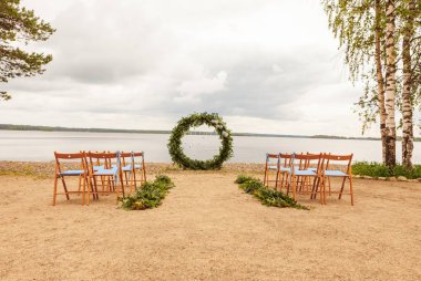 Güzel bir düğün ayarlandı. Düğün töreninin alanı. Yuvarlak kemer, çiçeklerle süslenmiş kahverengi sandalyeler, yeşillikler. Sevimli, modaya uygun rustik dekor. Şenlikli dekor, çiçek düzenleme parçası.