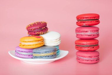 Beyaz bir tabak kurabiye yanında şık bir mercan arka plan üzerinde bir yığın pembe macaroons