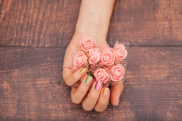 Hermosas manos femeninas con manicura moderna y flores rosadas sobre un fondo de caoba con tinte —  Fotos de Stock