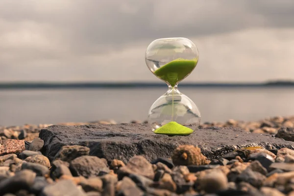 Zandloper met groen zand op het meer, staan op kleine stenen. Time concept — Stockfoto