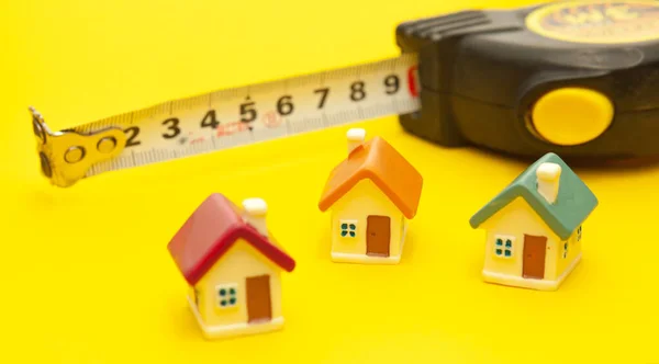Building tape measure and miniature houses on a yellow background, concept of building a house