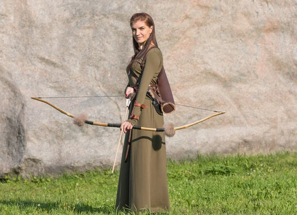 Woman with bow and arrow on the background of a stone wall