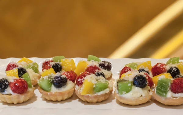 mini tarts with cream and berries. Delicious mini tarts with fresh berries and custard on table. Set of mini cakes in assortment on white plate. Restaurant menu. Variety of sweet mini desserts,