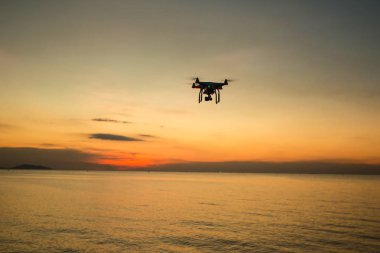 Gün batımının arka planında siluet drone. Akşam gökyüzünde uçan dronlar. Dijital kameralı Uav Drone. Uçan kamera bir fotoğraf ve video çeker. Kameralı drone kameranın fotoğrafını çeker.