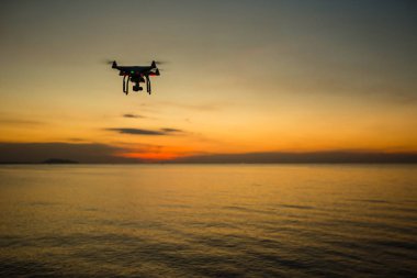 Gün batımının arka planında siluet drone. Akşam gökyüzünde uçan dronlar. Dijital kameralı Uav Drone. Uçan kamera bir fotoğraf ve video çeker. Kameralı drone kameranın fotoğrafını çeker.