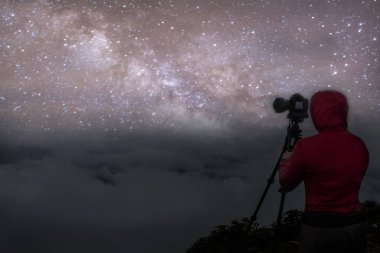 Taşın üzerinde duran bir adamın yıldızları ve silueti olan renkli bir gece göğü. Dağda bir adamla mavi samanyolu. Yüksekkayalar. Galaksisi ve silueti olan bir adam.. 