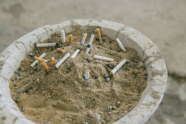 Kum kül tablasında bir sürü sigara koçanı. Sigaraların geri kalanı kül tablasında. Kül tablasında kumun üzerinde bir sürü sigara izmariti vardır. Bir sigara sağlık için iyi değildir.. 