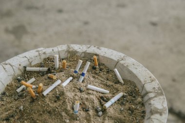 Kum kül tablasında bir sürü sigara koçanı. Sigaraların geri kalanı kül tablasında. Kül tablasında kumun üzerinde bir sürü sigara izmariti vardır. Bir sigara sağlık için iyi değildir.. 