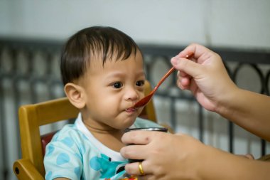Anne bebeği kaşıkla besliyor. Anne evde onun sevimli çocuğa sağlıklı yiyecek veren. kadın bebek yemek ve oturma veren