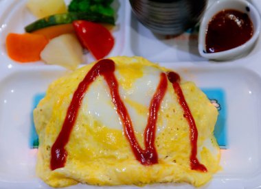 Çocuk için belirlenen pirinç menüsü üzerinde Tay omlet. Kızarmış yumurta (omlet), beyaz plaka üzerinde kaşık ve çatal ile Pilav. Üst görünüm Tayland tarzı Omlet pirinç. Pirinç üzerine pastırma ve mantar ile Kremsi omlet.
