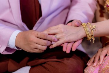 Evlilik yüzükleri. Alyansı ona taktı. Damat, yüzüğü geline tak. Tayland düğün töreni ve Tayland düğün süsü. Damat, yüzüğü gelinin parmağına tak..