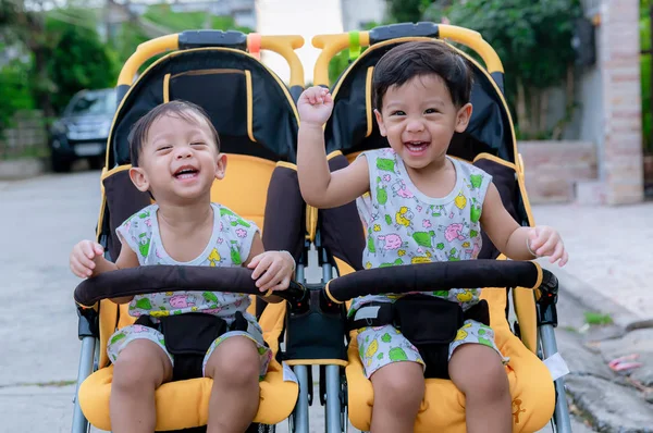 Two brothers sit in a stroller. Adorable twin baby boys sitting in stroller and smiling happily. Childhood emotions. Nursing twins