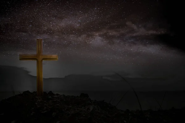 Cross wooden raised to the glory of God, Jesus Christ. Night light lighting a fire on a background of stones under the stars of the Milky Way.